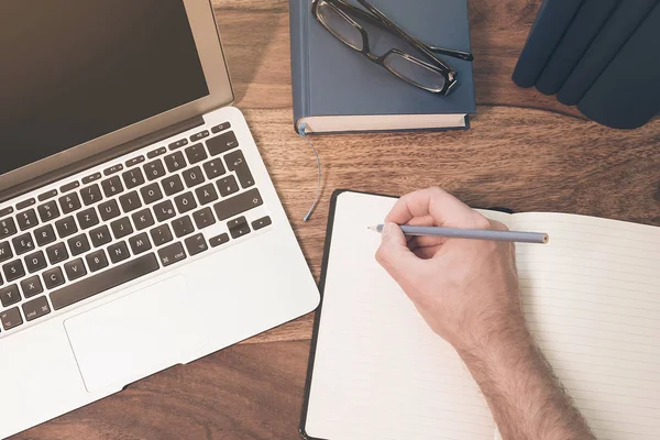 bir not defteri altında ahşap bir masaüstü üzerinde bir dizüstü bilgisayar üzerinde notlar alarak bir erkek kişi el Üstten Görünüm