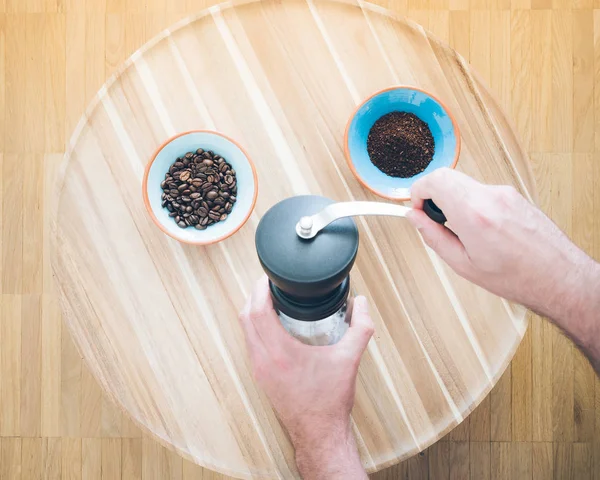 顶视图的操作手动咖啡研磨机和两碗咖啡豆与木制表面的研磨咖啡的男性手 — 图库照片