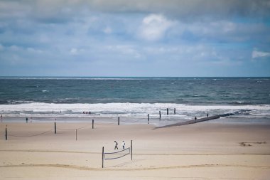 people on wide sand beach at north sea in stormy weather  clipart