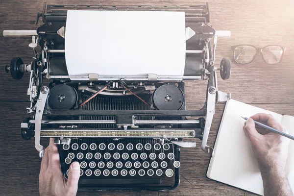 Top view of man taking notes besides vintage manual typewriter on rustic wooden table — Stock Photo, Image