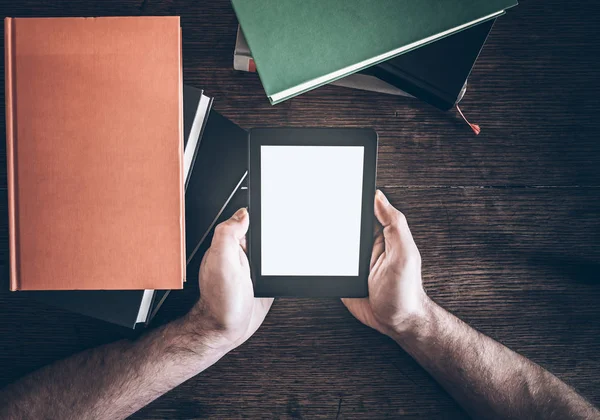 Manos del hombre sosteniendo lector de libros electrónicos entre pilas de libros sobre mesa de madera rústica — Foto de Stock