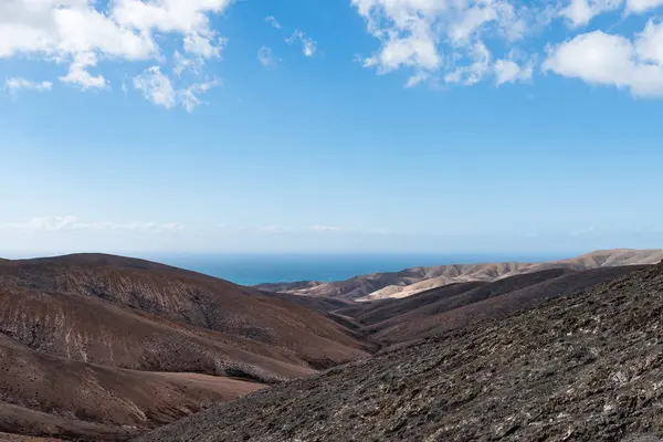 Paisagem rolante árida com oceano no fundo sob o céu azul em Fuerteventura — Fotografia de Stock