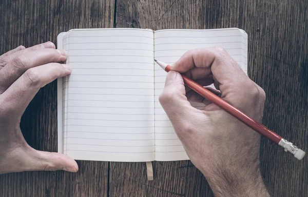 Vista superior del hombre sosteniendo el lápiz para escribir en el bloc de notas en el escritorio de madera —  Fotos de Stock