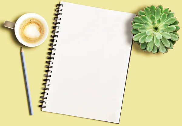 Spiralblock på gult skrivbord med penna, krukväxt och kaffemugg — Stockfoto