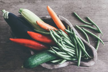 Çiğ mevsimlik sebzelerle dolu ahşap kâse manzarası.