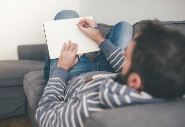 Adam kanepeye uzanmış not alıyor, günlük ya da defter yazıyor.