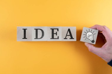 top view of wooden toy blocks with word IDEA and light bulb icon against orange background