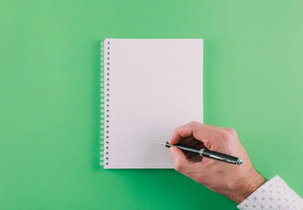 Top view of hand holding ballpoint pen against spiral notepad on green background — 图库照片