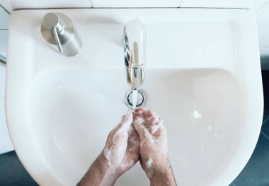 Banyo lavabosunda ellerini yıkayan kişinin üst görüntüsü.