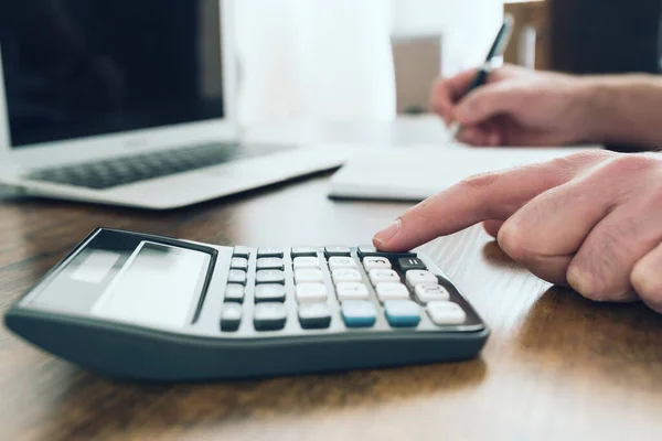 Close-up shot van persoon met behulp van pocket calculator tijdens het maken van aantekeningen — Stockfoto