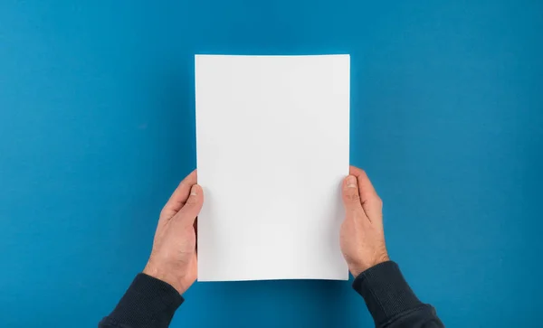 Direttamente sopra colpo di mani che tengono bianco foglio bianco di carta contro sfondo blu — Foto Stock