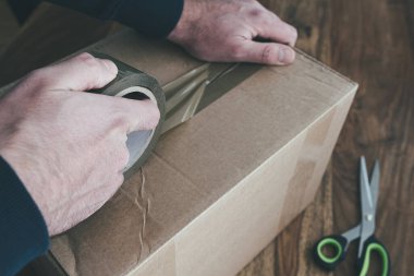 Paket bandıyla nakliye kutusunu mühürleyen kişinin yakın plan fotoğrafı.