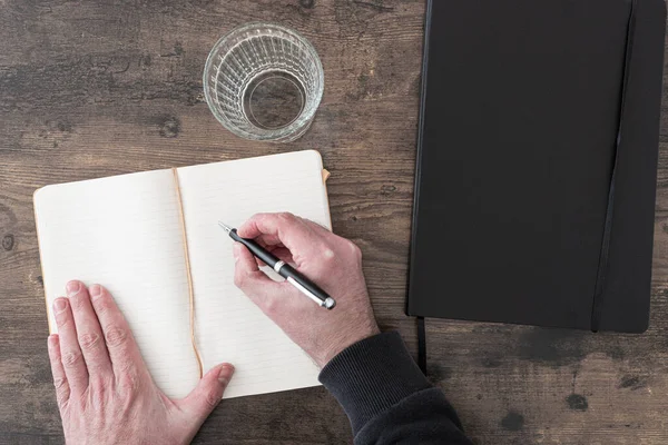 Vista anterior de la persona en el escritorio de madera tomando notas en el diario o diario — Foto de Stock