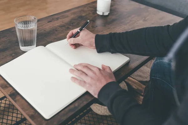 Rückansicht eines Mannes, der am Couchtisch sitzt und Tagebuch schreibt — Stockfoto