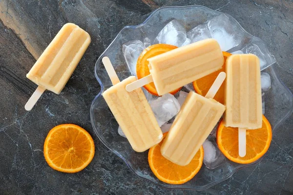 Ghiaccioli allo yogurt arancione in una ciotola piena di ghiaccio contro l'ardesia — Foto Stock