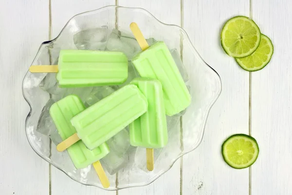 Lime yoghurt popsicles i en is fylld skål mot vitt trä — Stockfoto