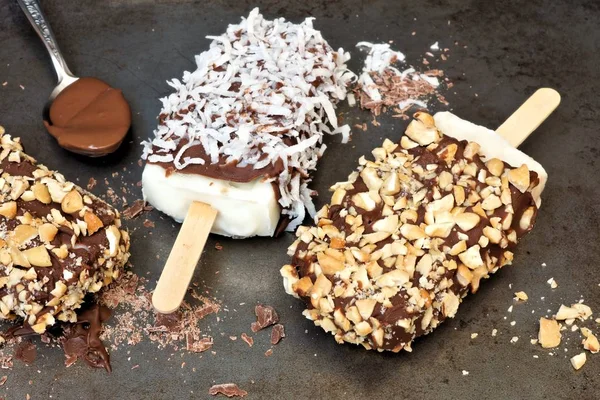 Coklat dicelupkan es dengan kacang dan kelapa terhadap latar belakang gelap — Stok Foto