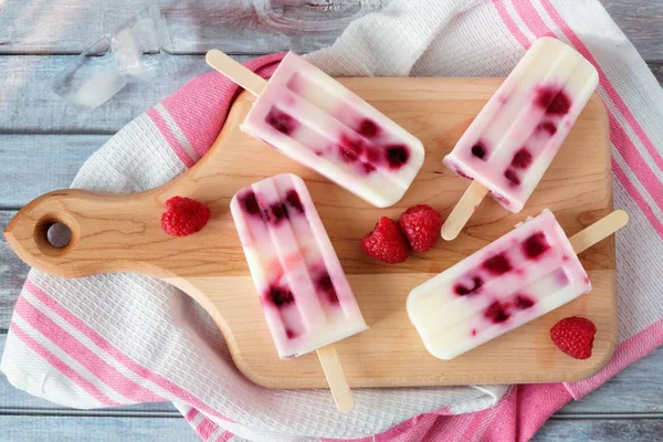 Raspberry vanilla ice pops on a paddle board against rustic wood