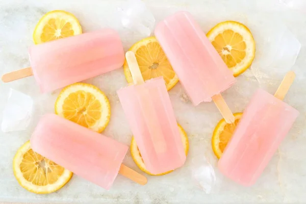 Pink lemonade popsicles with lemon slices, on white marble