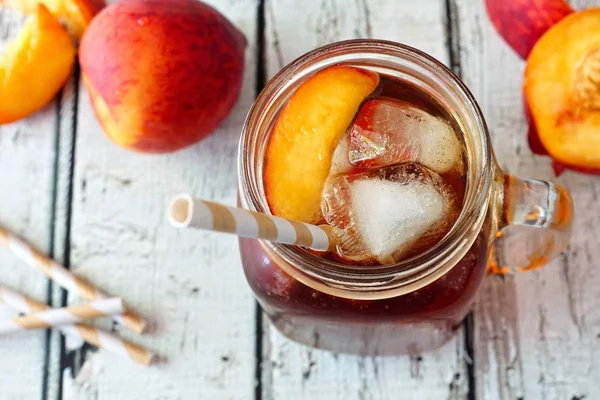 Mason jar of peach iced tea on rustic white wood, downward view — Stock Photo, Image