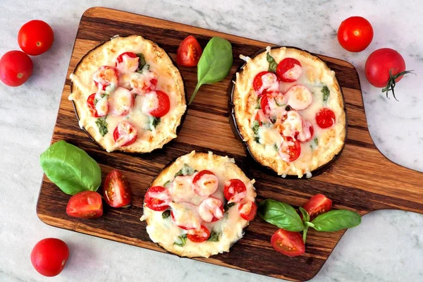 Mini pizze di melanzane con mozzarella, pomodori e basilico su un tagliere contro il marmo — Foto Stock