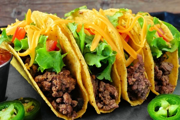 Hard shelled tacos with ground beef, lettuce, tomatoes and cheese close up