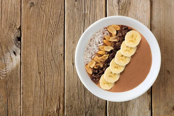 Peanut-butter, banana, chocolate smoothie bowl over rustic wood