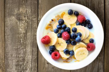 Breakfast cereal with blueberries, bananas and raspberries on wood clipart