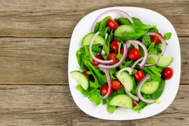 Salata yeşillikleri, cherry domates, kırmızı soğan ve ahşap üzerine salatalık ile
