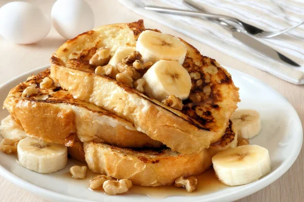 Plate of delicious French toast with bananas, walnuts and dripping maple syrup