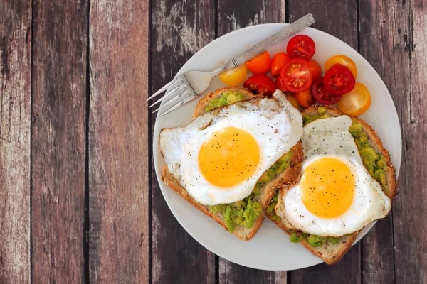 Aguacate saludable, tostadas de huevo en plato con tomates sobre madera rústica —  Fotos de Stock