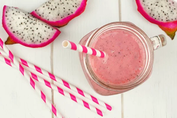 Pink raspberry, dragon fruit smoothie with fruit slices and straws on a white wood background, downward view