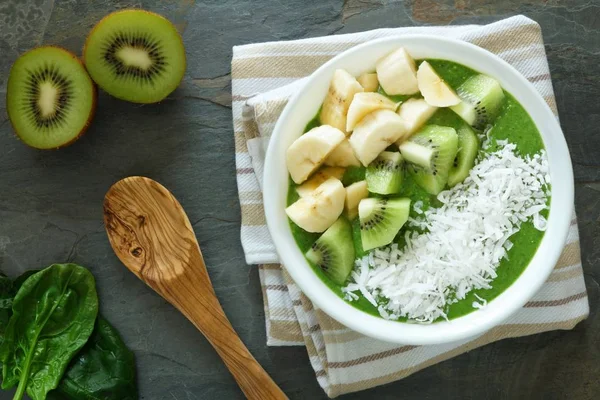 Green smoothie bowl with spinach, kiwi, bananas and coconut over slate