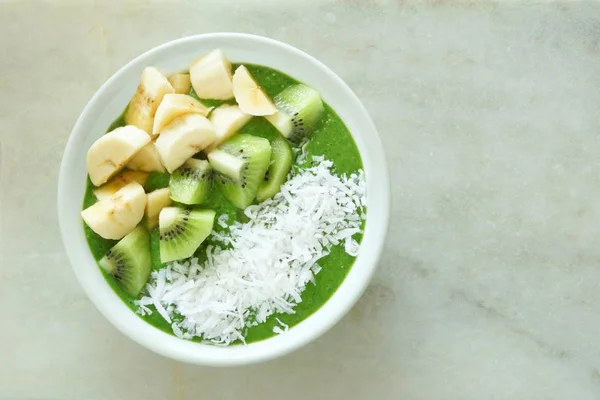 Green smoothie bowl over white marble