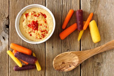 Baby rainbow carrots with hummus dip, overhead on a rustic wood clipart