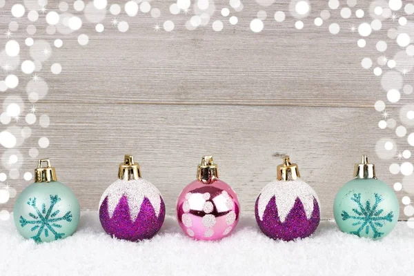 Purple, pink and turquoise Christmas baubles in snow against wood — Stock Photo, Image