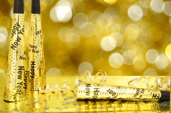 New Years Eve noisemakers and confetti with twinkling gold light background
