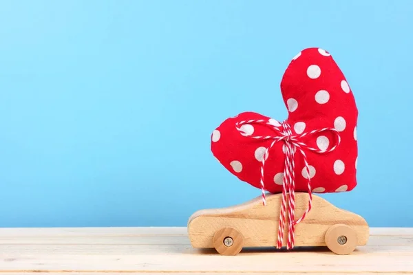 Wooden toy car carrying homemade heart gift against a blue background. Valentines Day or love concept.