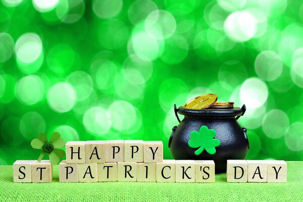 Happy St. Patricks Day wooden blocks with Pot of Gold and shamrock over twinkling green background
