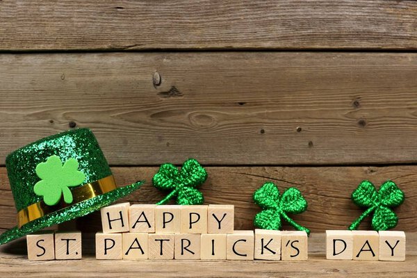 Happy St. Patricks Day wooden blocks with shiny shamrocks and leprechaun hat on a wooden background

