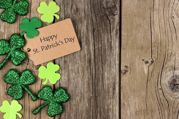 Happy St. Patricks Day tag with side border of shiny shamrocks over a rustic wood background
