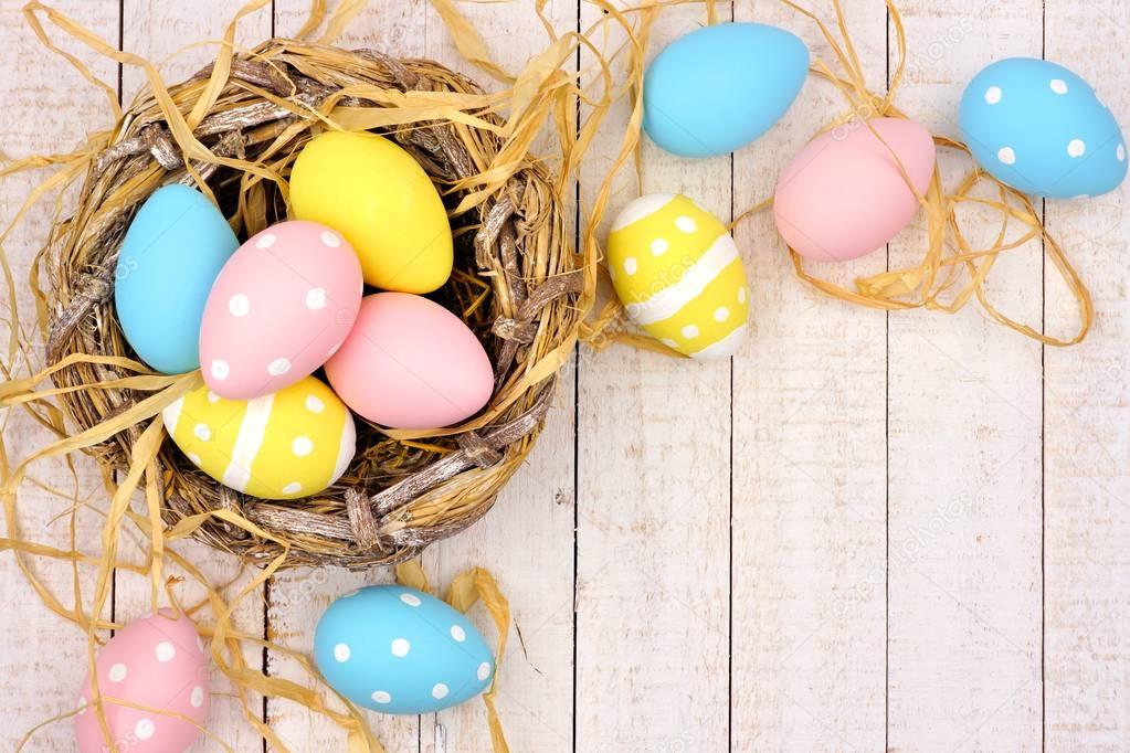 Springtime nest with pink, yellow and blue painted Easter Eggs. Corner border against a rustic white wood background.