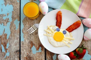 Sevimli tavşan kahvaltıyla Paskalya yumurta ve domuz pastırması yüz yaptı. Rustik bir mavi ahşap arka plan üzerinde görünümünün üst tablo sahne.