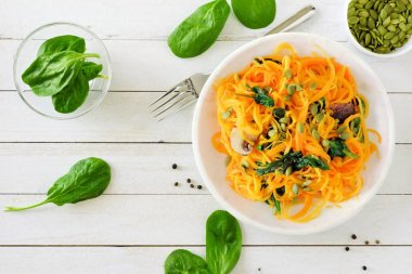Beyaz ahşap arka planda, kavram yeme sağlıklı ıspanak ve balkabağı tohumları ile butternut squash spirilized erişte. Üstten Görünüm, tablo sahne.