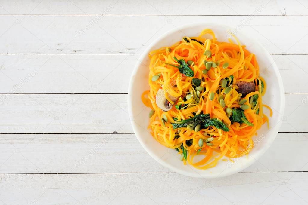 Butternut squash spirilized noodles with spinach and pumpkin seeds on white wood background, Healthy eating concept. Top view.
