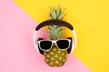 Güneş gözlüğü ve kulaklık ile hippi ananas. Üstten Görünüm sarı ve pembe bir arka plana dayanır. En az yaz konsepti.