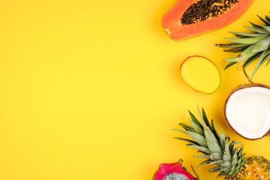 Tropical fruit side border with pineapple, dragon fruit, papaya, coconut and mango on a bright yellow background clipart