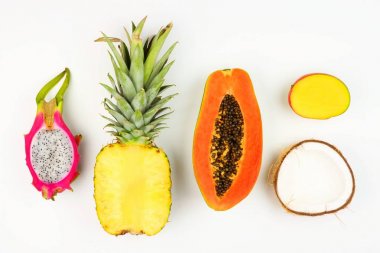 Tropical fruit flat lay with cut pineapple, dragon fruit, papaya, mango, and coconut on a white background clipart