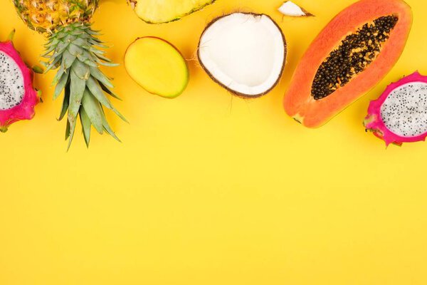 Tropical fruit top border with pineapple, dragon fruit, papaya, coconut and mango on a bright yellow background