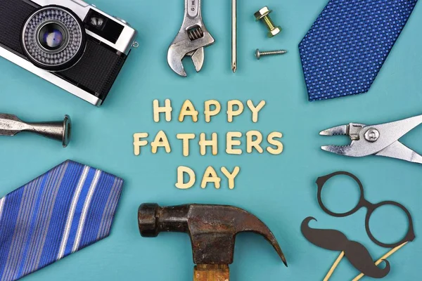 Happy Fathers Day message with frame of gifts, decor, ties and tools on a blue background. Top view.